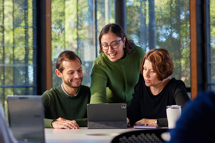 3 students look at a laptop in a UQ learning space